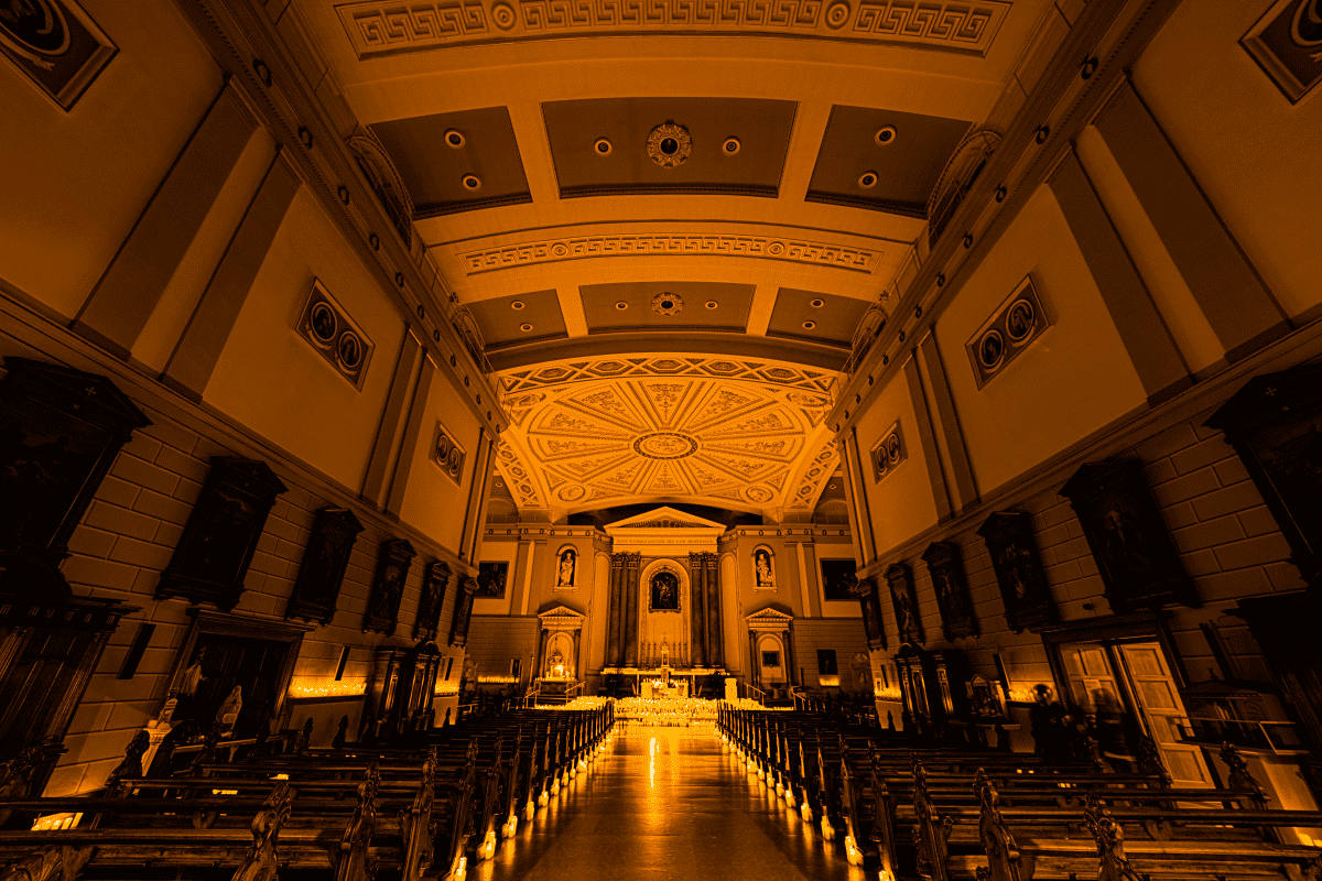 A wide shot of the inside of St Andrew's Parish Church showing the pews lined by candles and the altar covered in candlelight.