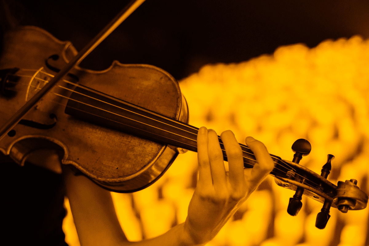 A close-up of a violin being played with the blurry image of candlelight.