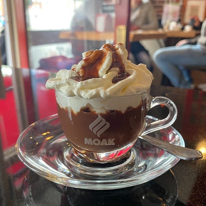 A translucent glass filled with hot chocolate and whipped cream.