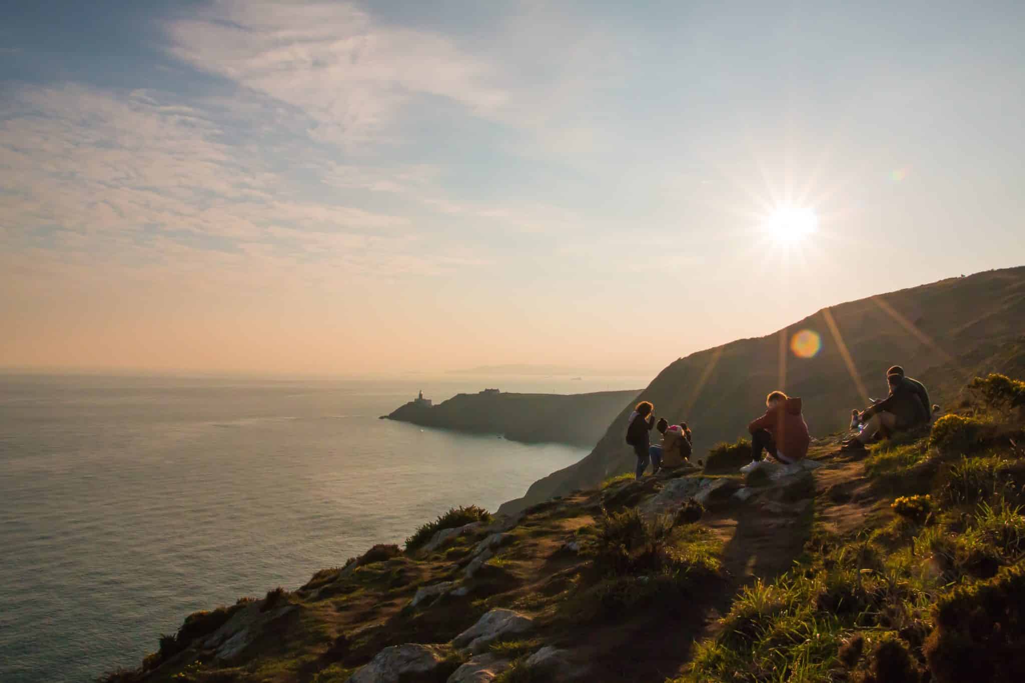 People sitting on the edge of a cliff looking at the views before sunset in Howth, a viewpoint in Dublin.