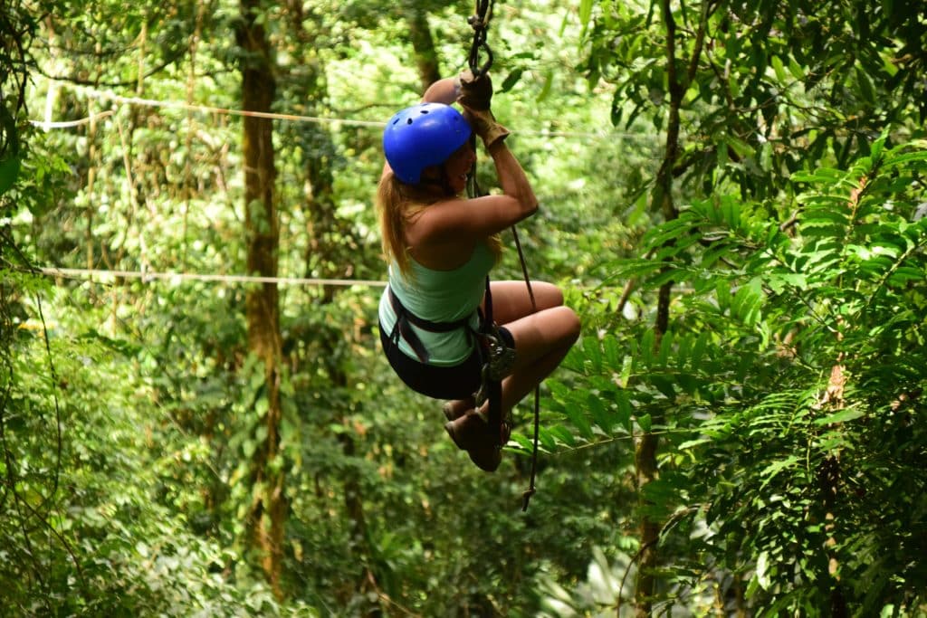 A woman in a blue helmet rides a zipwire in a forest.